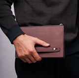 Hand holding slim leather travel pouch at airport security, passport partially visible in slot