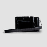 Black Leica camera with leather strap on a light gray background