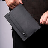 Person holding a black leather clutch bag against a neutral background