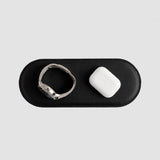 Black leather case with a smartwatch and white earbuds on a light gray background