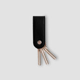 Key organizer with black leather strap and metallic keys on a light gray background